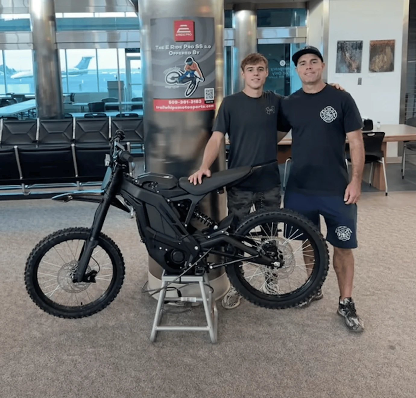 Micah (left) and his dad Jason (right), the father-and-son team behind TrailWhip eMotosports, standing with an E-Ride Pro electric dirt bike